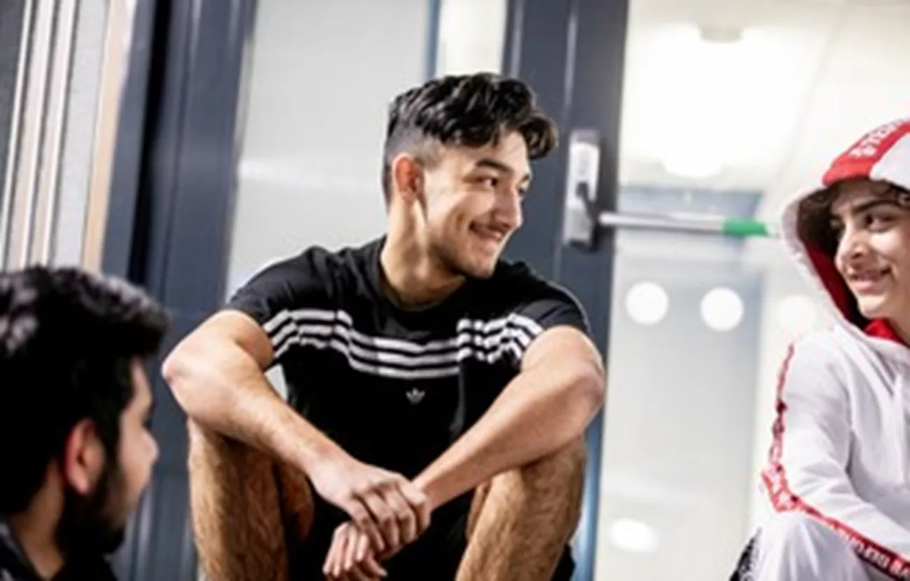 Tre unga killar syns på bilden. De sitter avslappnade och ler mot varandra.