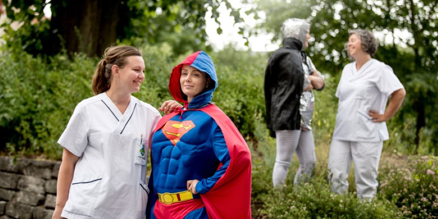 Kvinna iklädd superhjältedräkt pratar med en kollega som är iklädd vårdkläder.
